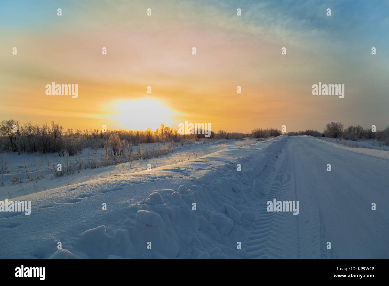 Winter road with snowy roadsides passing through the floodplain with traces of the protector at dawn Stock Photo