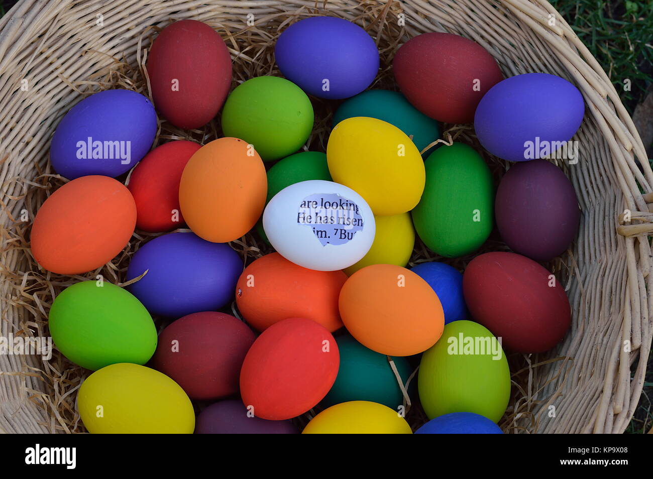 bright white egg with broken shell and Bible text in the words: HE HAS RISEN in the midst of many colorful Easter eggs Stock Photo