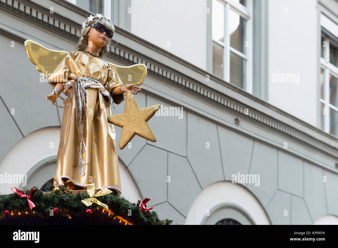 A statue of a cute little angel in a gold and silver robe, holding a star and wearing cool sunglasses on top of a christmas market booth. Stock Photo