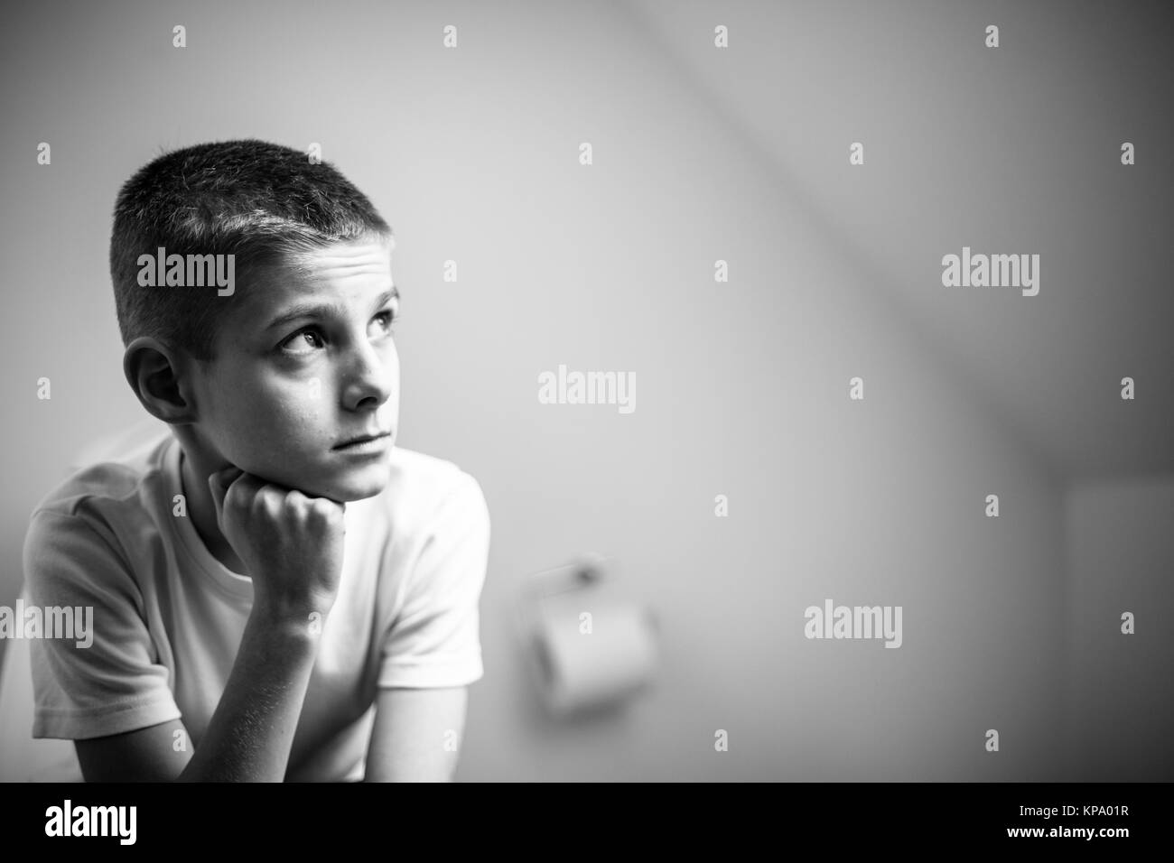 Contemplative Boy Sitting on Toilet in Monochrome Stock Photo