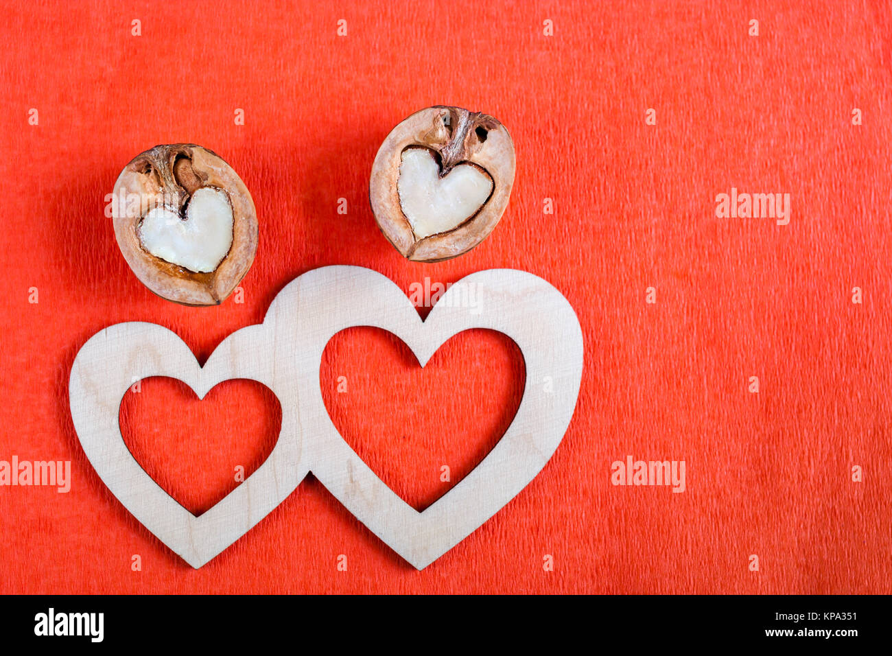 Two carved wooden hearts and two halves of walnut in shape of heart  are lying on red textured paper background and copy space. Top view. Stock Photo