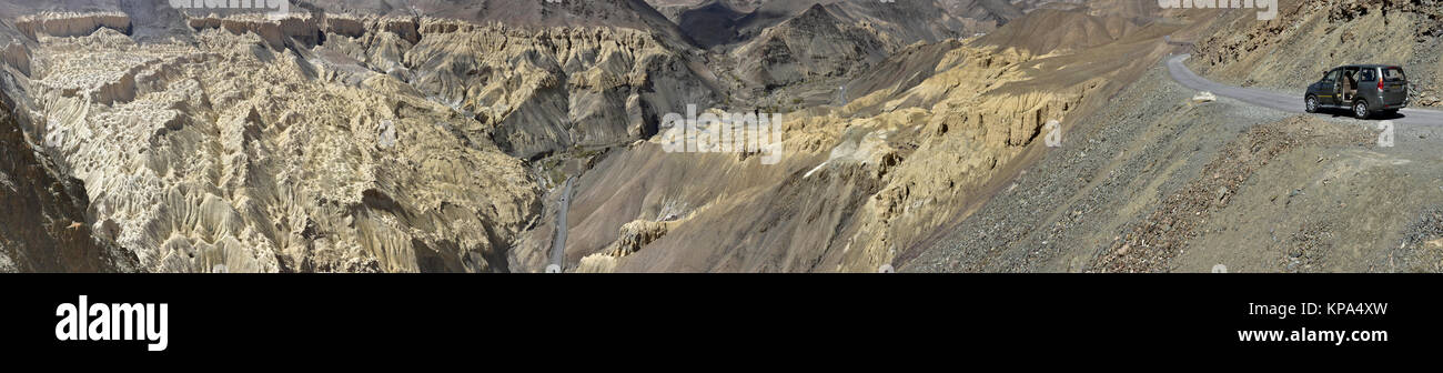 Black car on a mountain road, the route runs along the edge of the cliff above the huge yellow rocks, the Himalayas, a photo panorama. Stock Photo