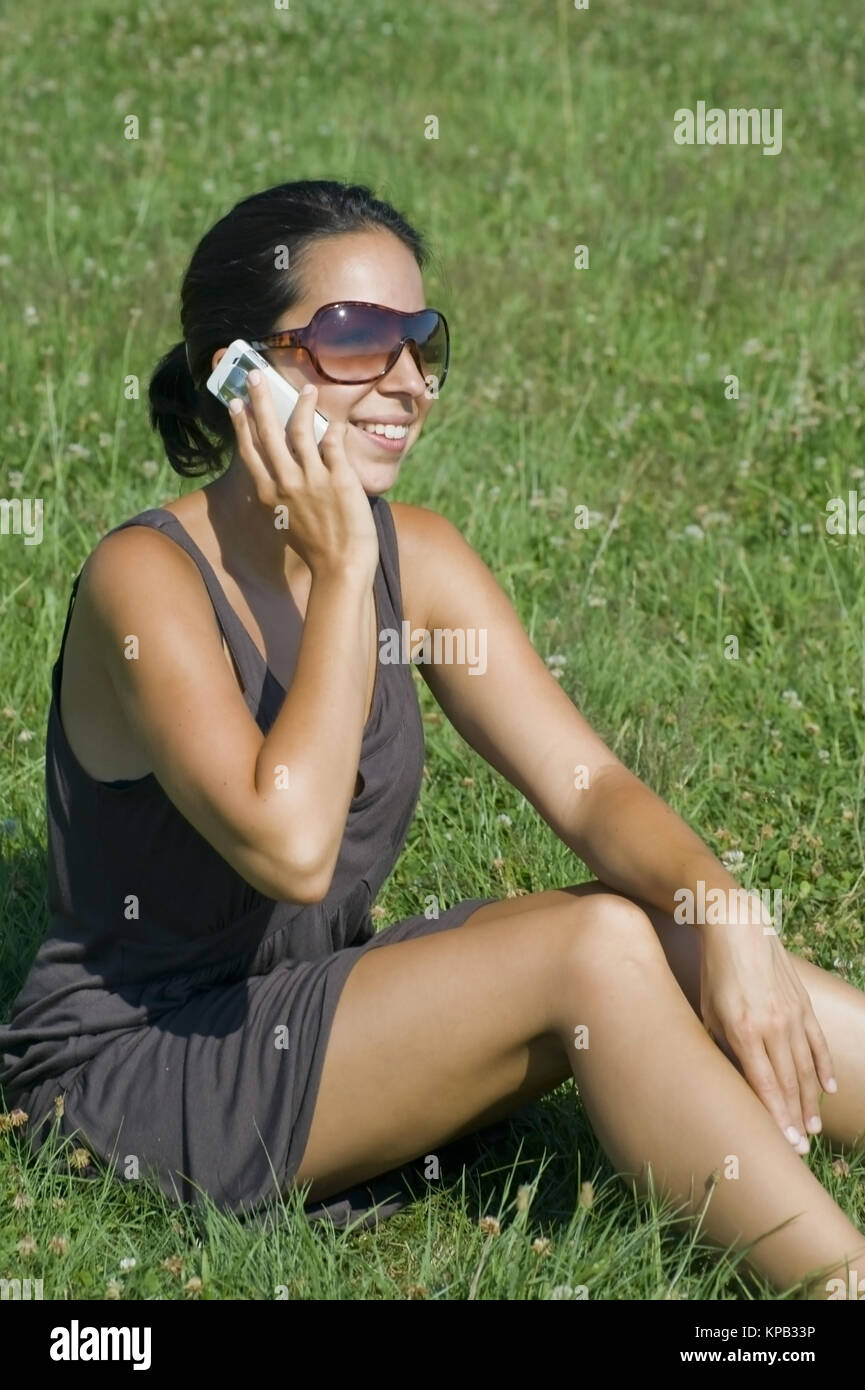 Model release, Junge Frau sitzt in Wiese und telefoniert mit Handy - woman with mobile phone in meadow Stock Photo