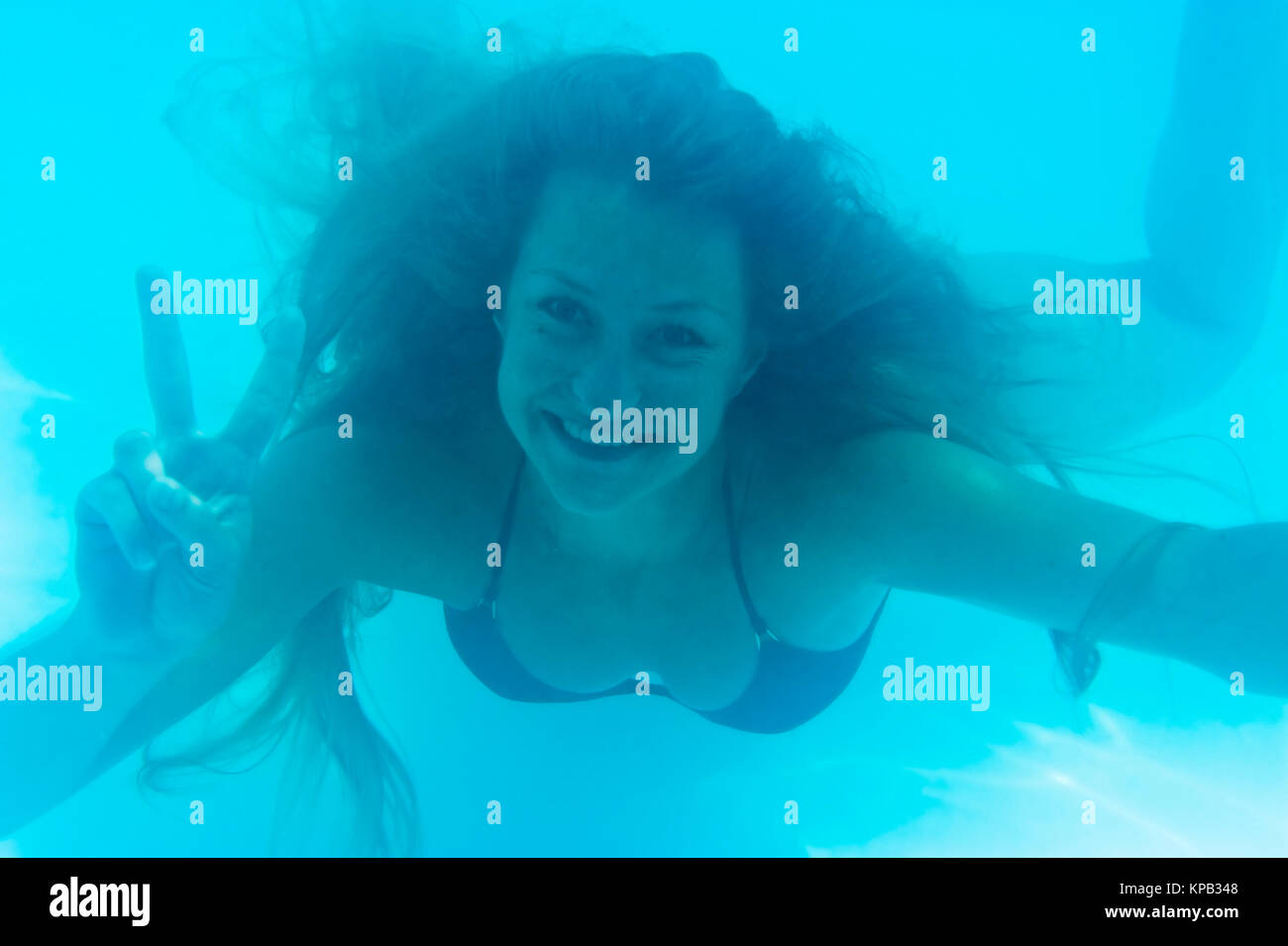 Model release, Junge Frau schwimmt unter Wasser und macht Fingerzeichen - woman under water Stock Photo