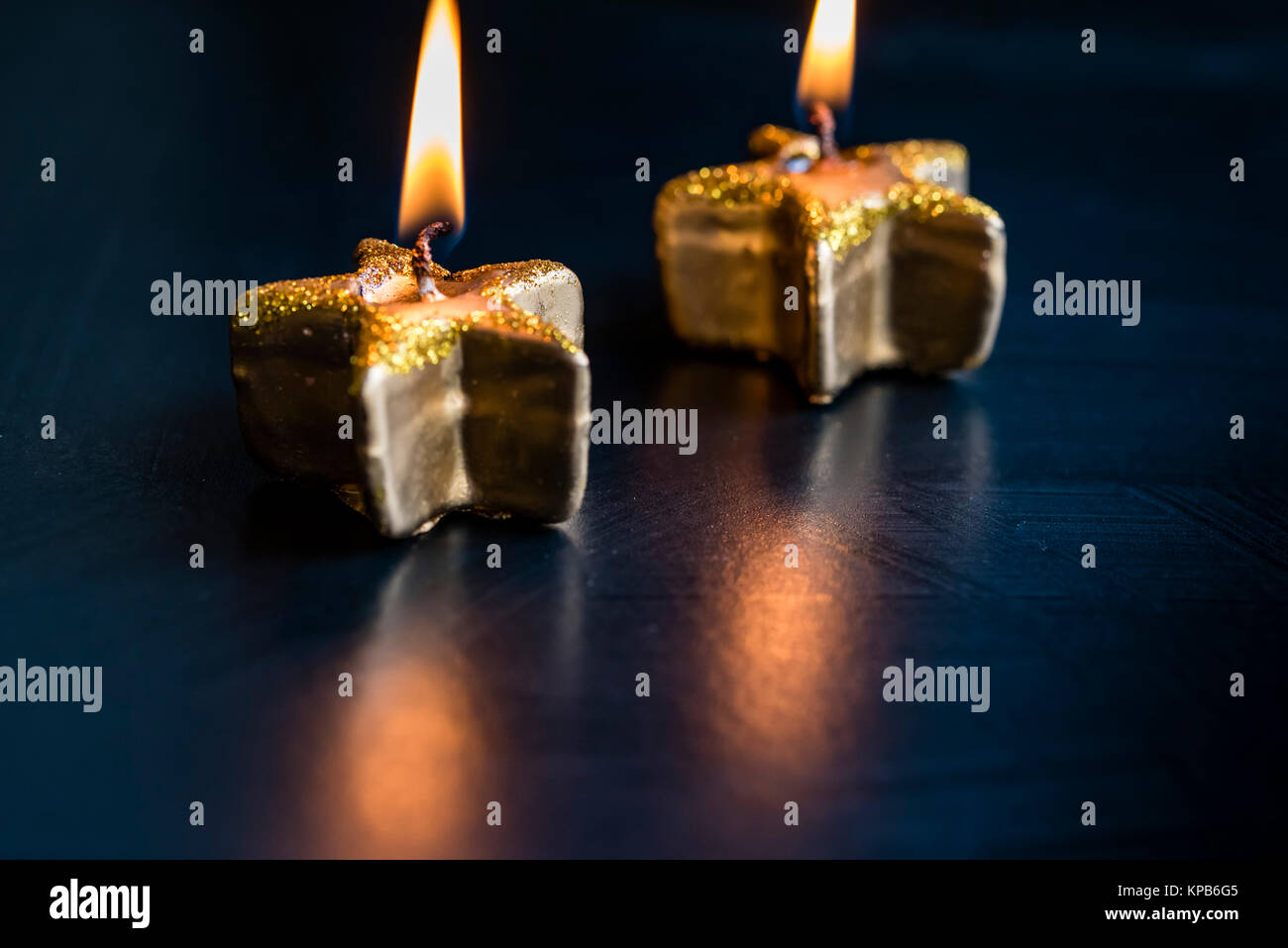 Lit golden Christmas candles on black, macro, room for copy. Festive burning candles, star shaped, shimmering bokeh. Stock Photo