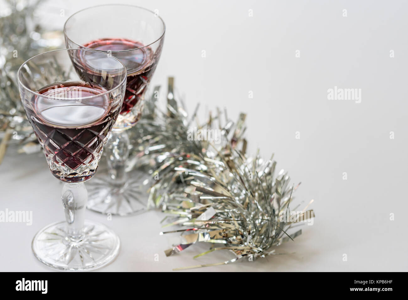 Glasses of red wine, silver on white background, top view. Christmas festive theme, wine glasses, silver tinsel shines, room for text. Stock Photo