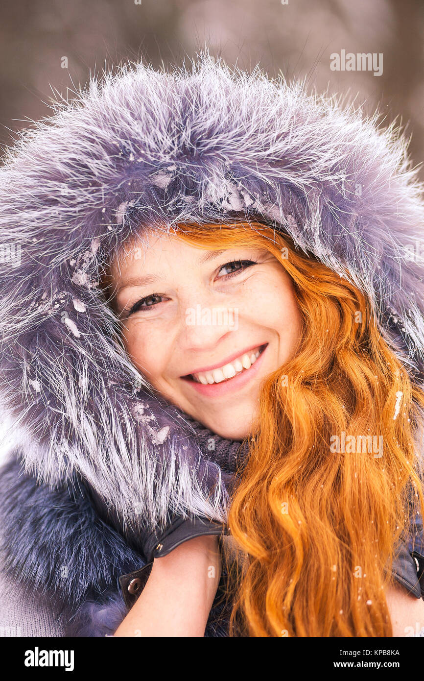 Portrait of beautiful young girl dressed in fur coat at winter trees background. Beauty woman having fun outside on snowy day. Close up of female smil Stock Photo