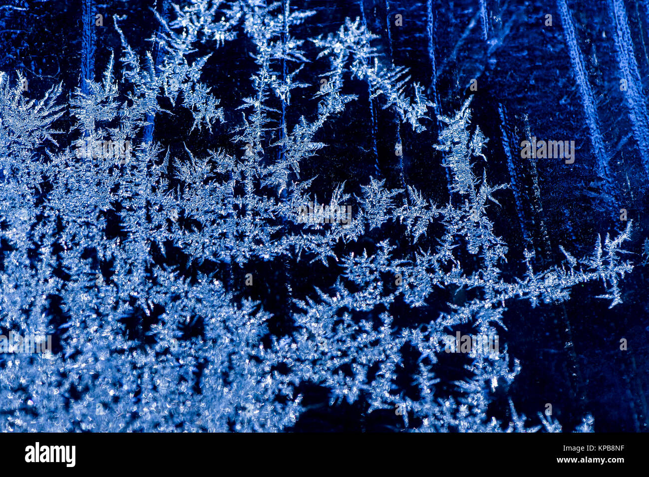 Ice crystals formed on window against a cold blue background Stock Photo