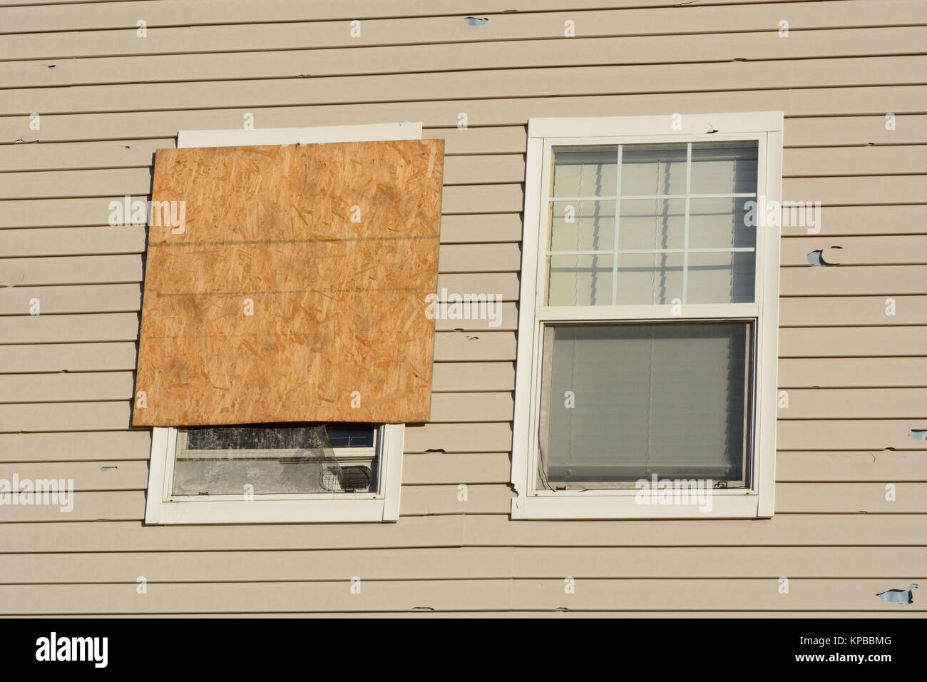 Boarded up window and hail storm damage on house siding and window frame Stock Photo