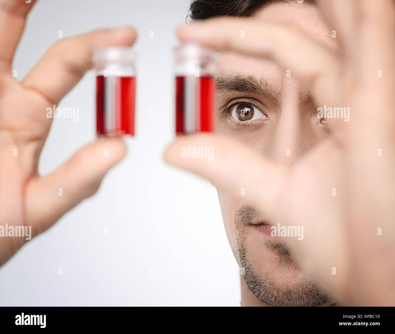 Young male medic or researcher holds up liquid samples. Shallow DOF, focus on the face. This image is toned. Stock Photo