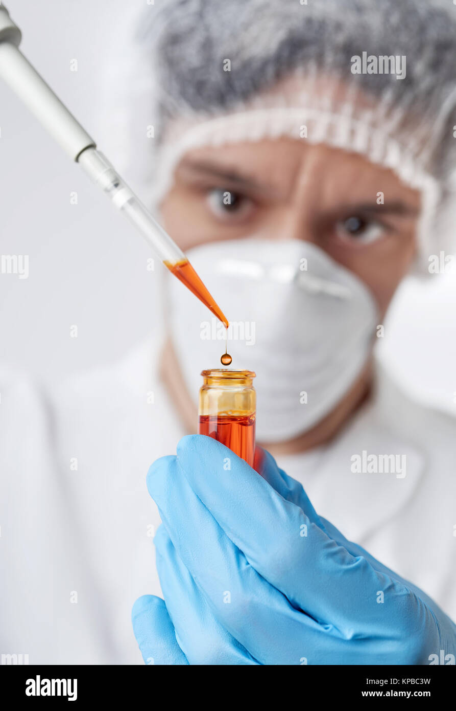 Keen scientist with brown eyes in protective wear pipettes orange sample Stock Photo