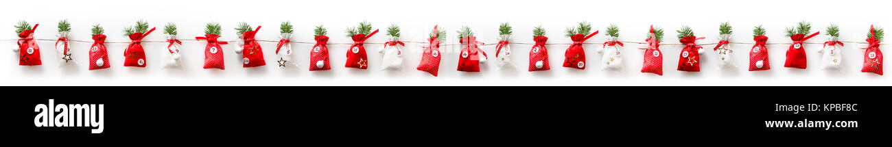 Advent calendar with twenty four red and white bags decorated with sprigs of pine on a white background to be opened one a day through December leading up to Christmas Stock Photo