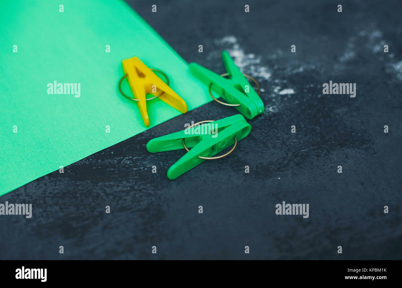 Fun housekeeping with yellow and green plastic clothes pegs. Bright composition of cleaning tools, dark concrete background. Space for your product di Stock Photo