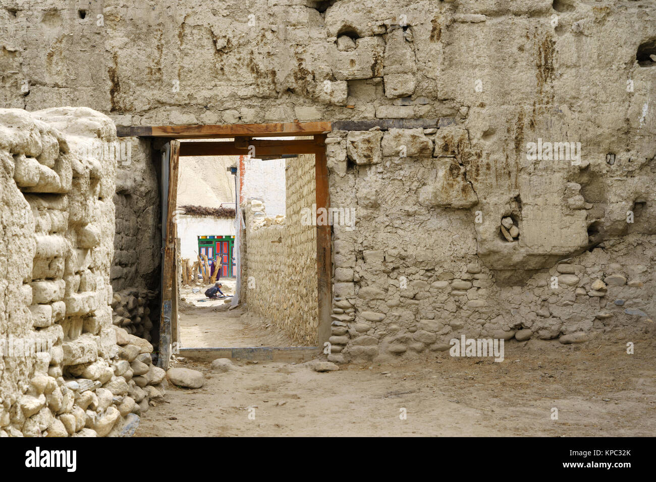 Seen through a passage, a Tibetan woman is washing clothes in the canal that supplies water to the inhabitants of Lo Manthang, Upper Mustang, Nepal. Stock Photo