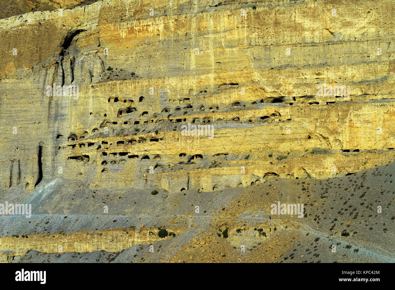Ancient cave dwellings carved in a gigantic cliff above Chuksang, Upper Mustang. Minuscule silhouette of a traveler visible on low right hand side. Stock Photo