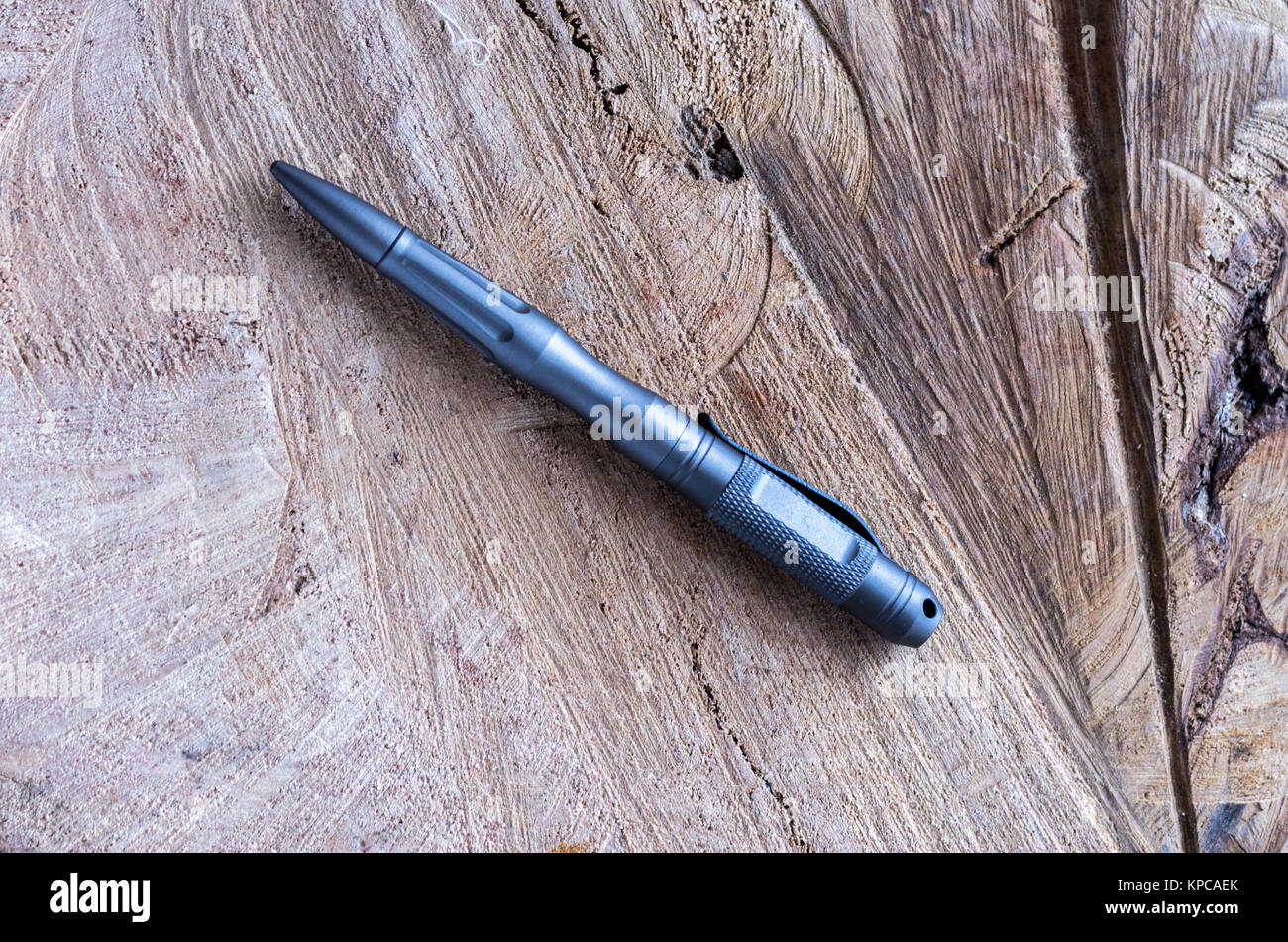 Gray metal handle for self-defense. Ballpoint pen made of metal. Wooden background from oak. Stock Photo