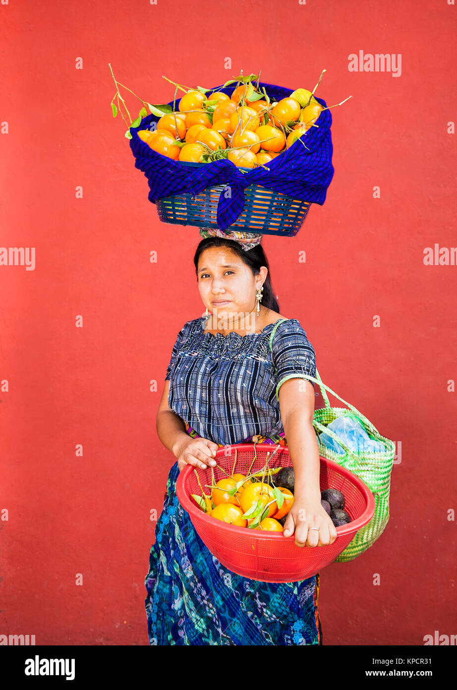 ANTIGUA, GUATEMALA - DEC 23, 2015; Unknown young Guatemalan woman carries fruit in a baskets at her head and hands on Dec 23, 2015, Antigua, Guatemala Stock Photo