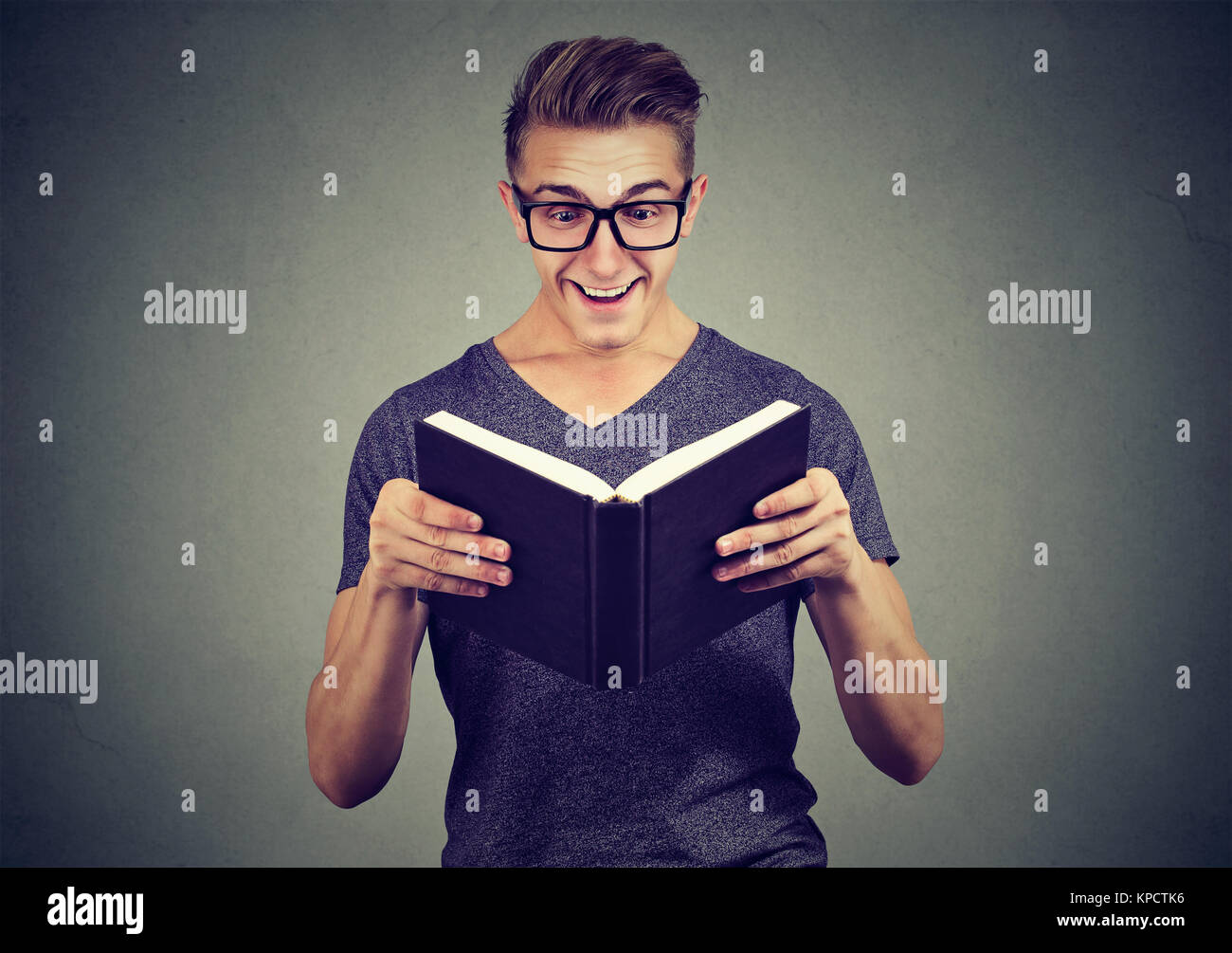 Smart man in eyeglasses reading book with great expression of happiness. Stock Photo