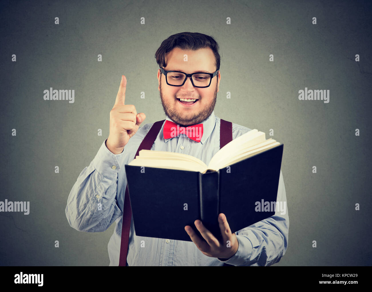 Young fleshy man in eyeglasses enlightened with new ideas inspired with book in hands. Stock Photo