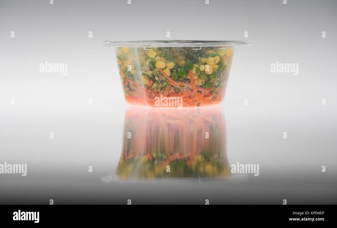 Ready made vegetables in plastic pot ready for eating on a white background, peas, sweet corn and carrots. Stock Photo