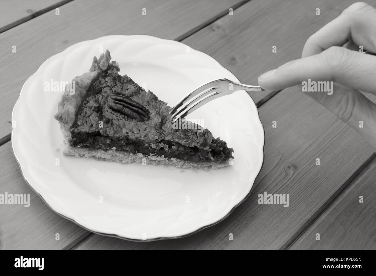 Woman uses dessert fork to cut into a slice of pecan pie Stock Photo