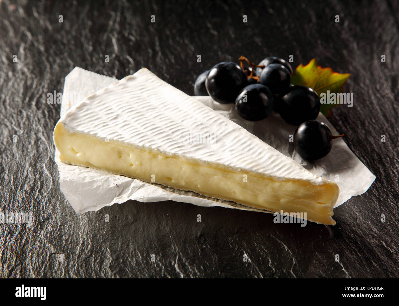Wedge of ripe brie cheese with a small bunch of black grapes served on ...
