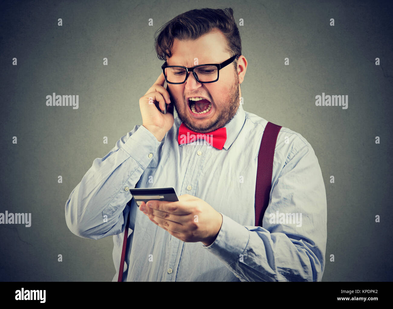 Discontent and irritated man clearing up issue with credit card while speaking on telephone. Stock Photo