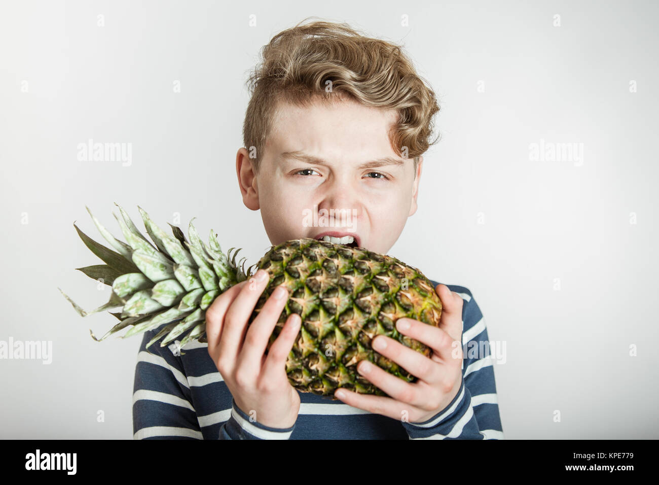 Boy Biting into Tough Skin of Pineapple Stock Photo