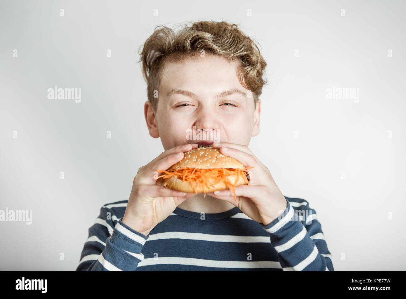 Boy Eating Burger Bun Topped with Shredded Carrots Stock Photo