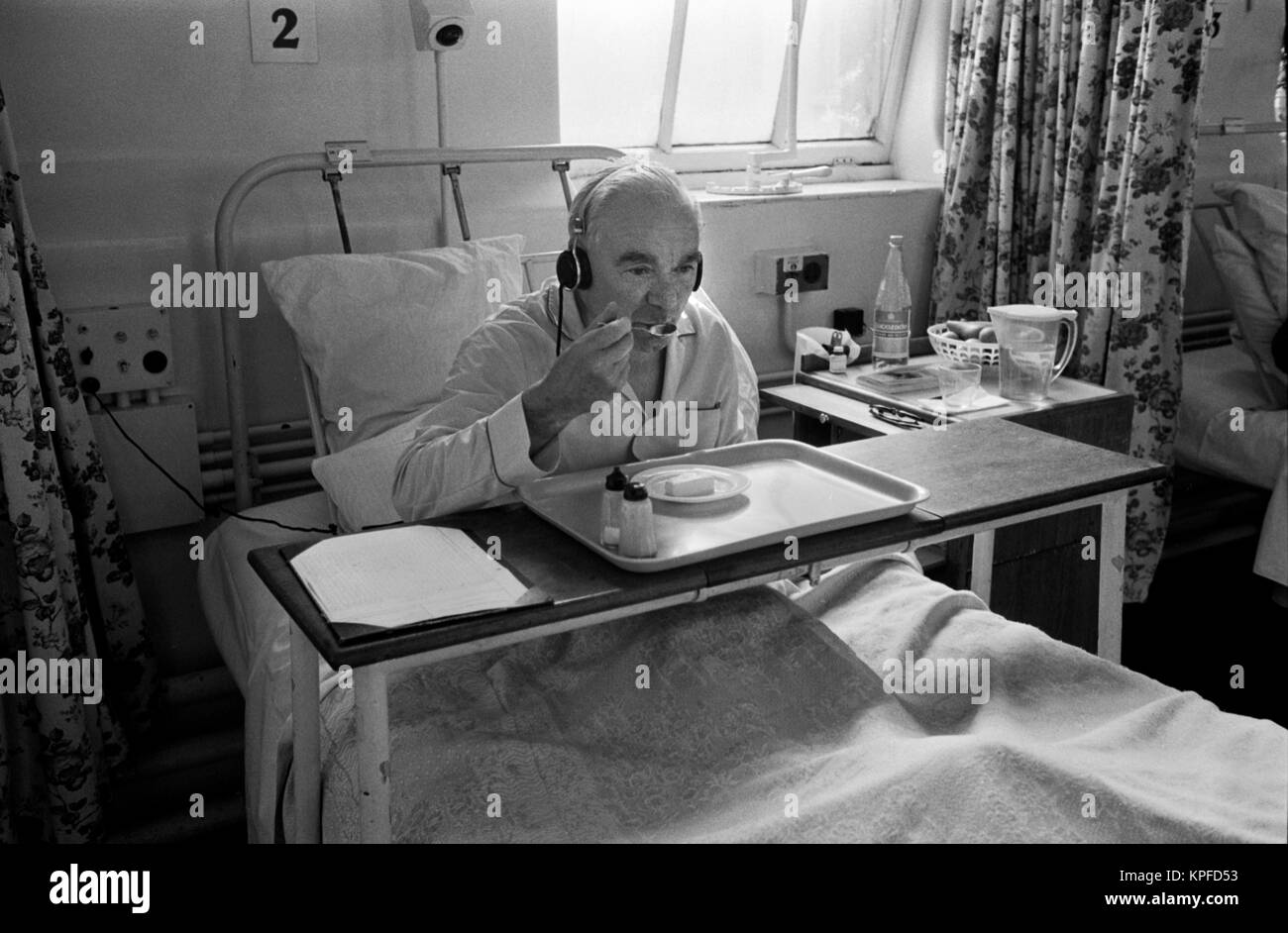 The 1970s National Health Service (NHS) Charing Cross Hospital. An older man sitting up in bed eating his lunch. He is listening to the radio and wearing headphones.  Fulham, London, England circa 1972. HOMER SYKES Stock Photo