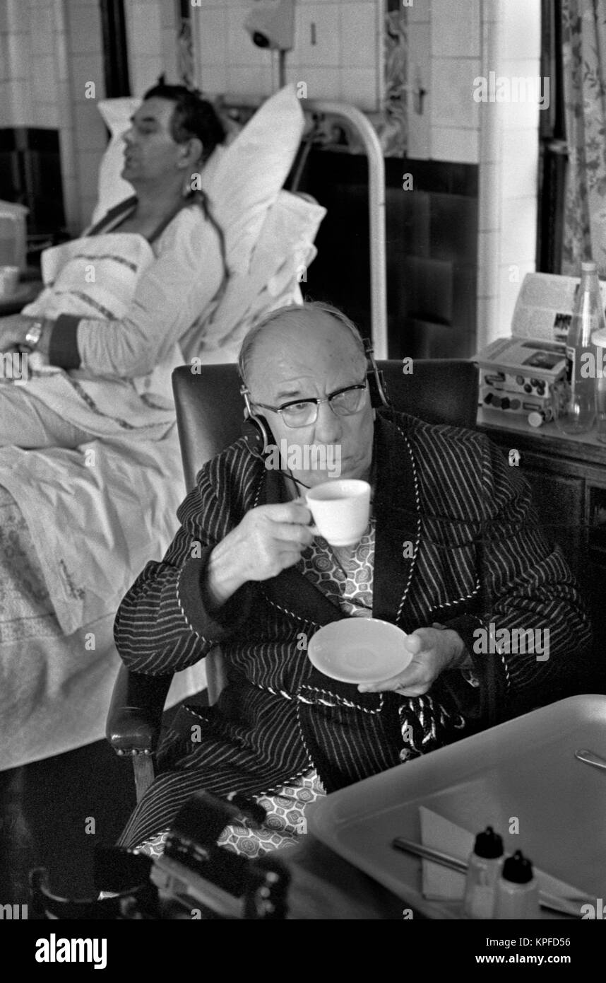The 1970s National Health Service (NHS) Charing Cross Hospital. An older man in his dressing gown and sitting in a chair drinking a cup of tea. He is watching the television and wearing headphones, so the TV volume does not have to be turned up to high. Fulham, London, England circa 1972. HOMER SYKES Stock Photo