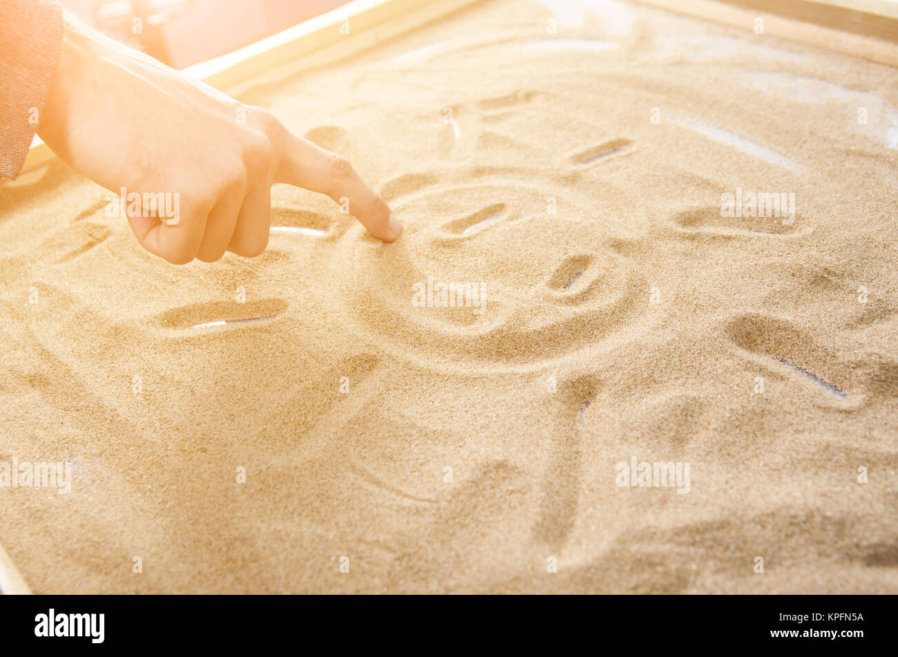 a man draws by his  finger on the sand symbol of the smiling sun. toned. Stock Photo