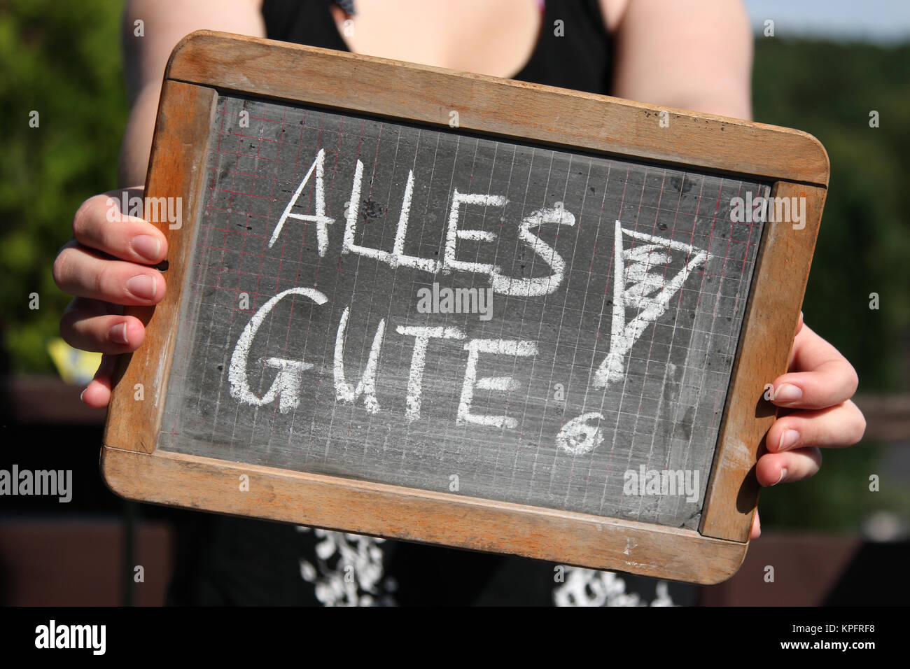 ALLES GUTE (all the best in German) written with chalk on slate shown by young female Stock Photo