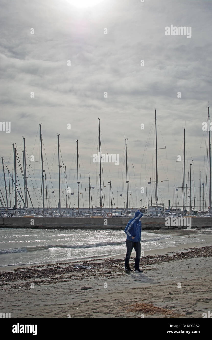 PLAYA DE PALMA, MALLORCA, SPAIN - DECEMBER 14, 2017: Young man in hood sweater walks on the winter beach on a windy day on December 14, 2017 in Mallor Stock Photo