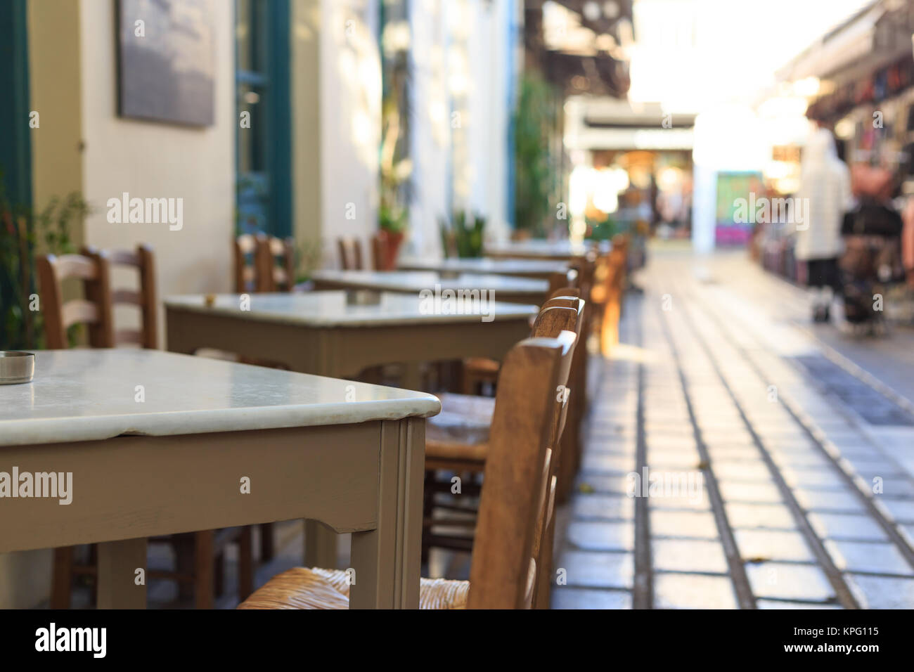Athens, Greece. Greek tavern empty tables and chairs in a row, blur pedestrian and market background Stock Photo