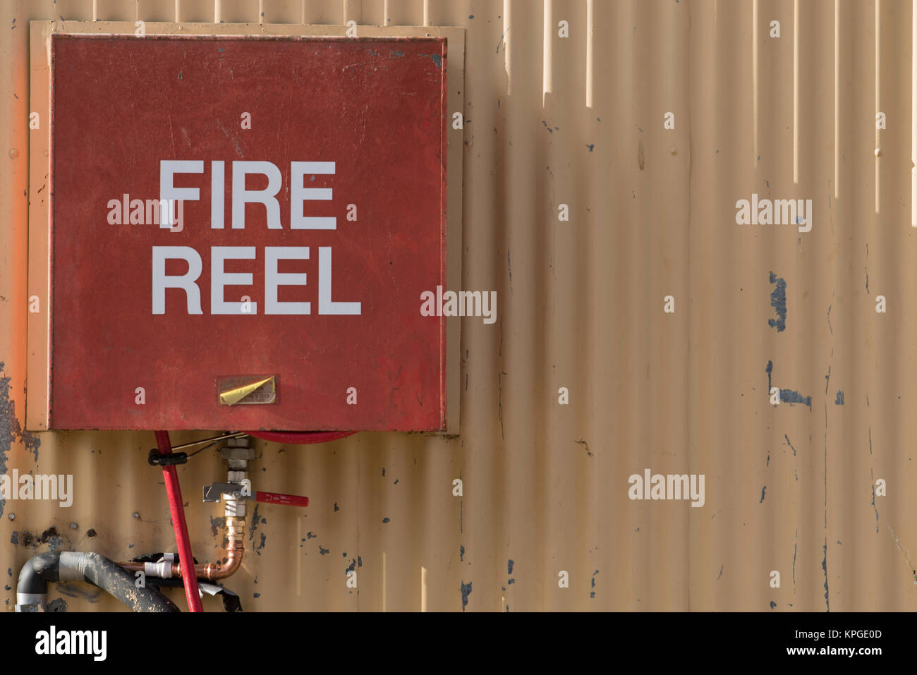 An old fire hose reel mounted on a corrugated iron wall in the afternoon light Stock Photo