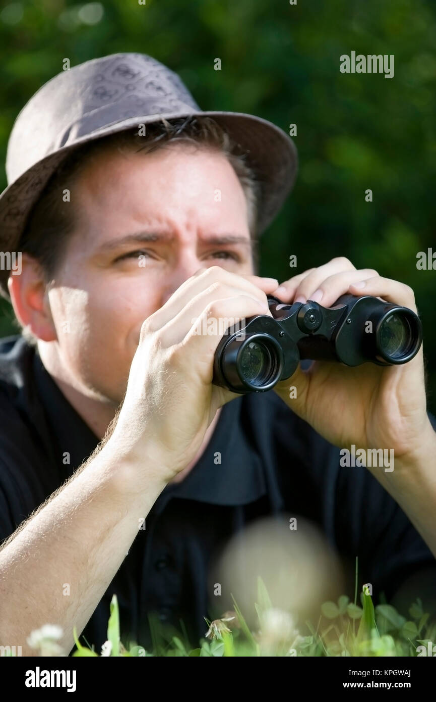 Model released , Junger Mann mit Fernglas in der Wiese - man with spy glass in meadow Stock Photo