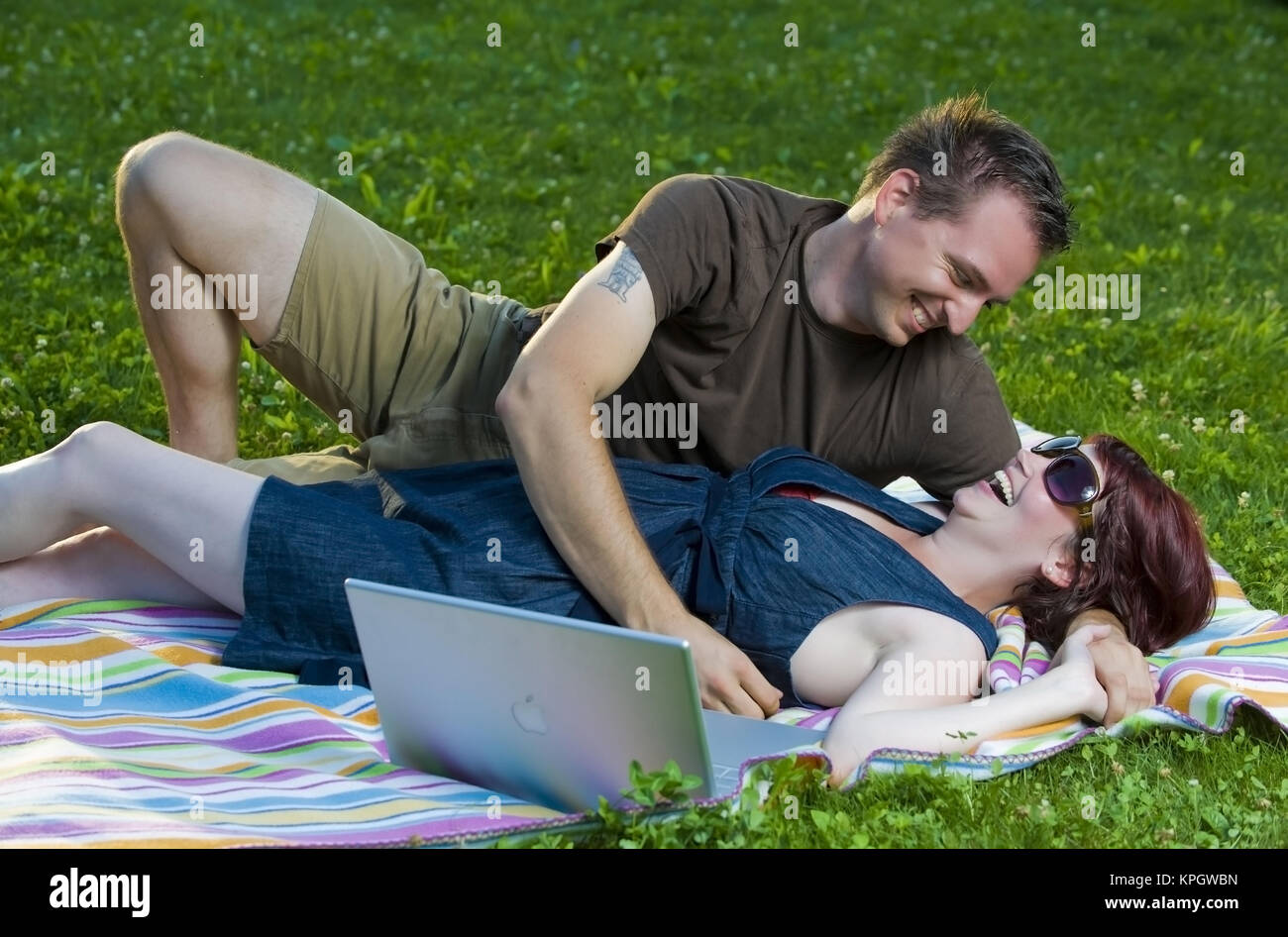 Model released , Junges Paar liegt mit Laptop auf einer Decke in der Wiese - couple with laptop lying in meadow Stock Photo