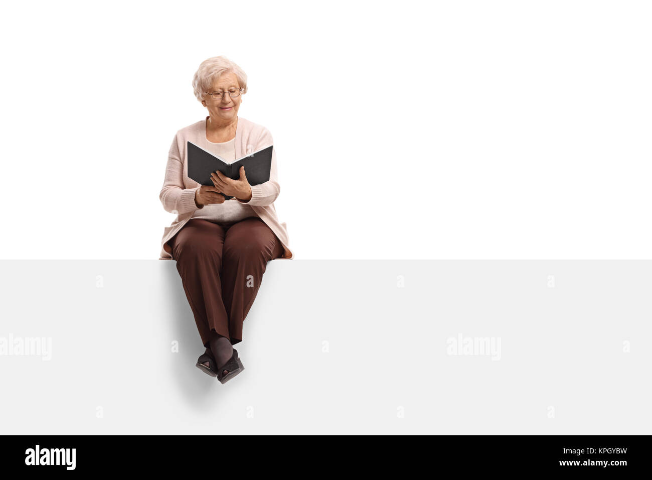 Elderly woman sitting on a panel and reading a book isolated on white ...