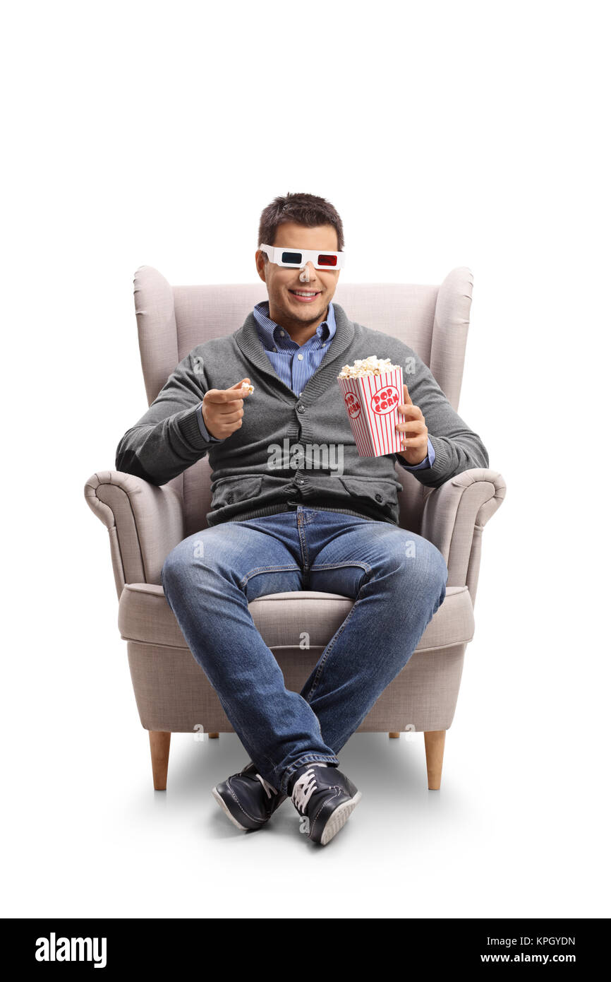 Young man wearing a pair of 3D glasses sitting in an armchair and having popcorn isolated on white background Stock Photo