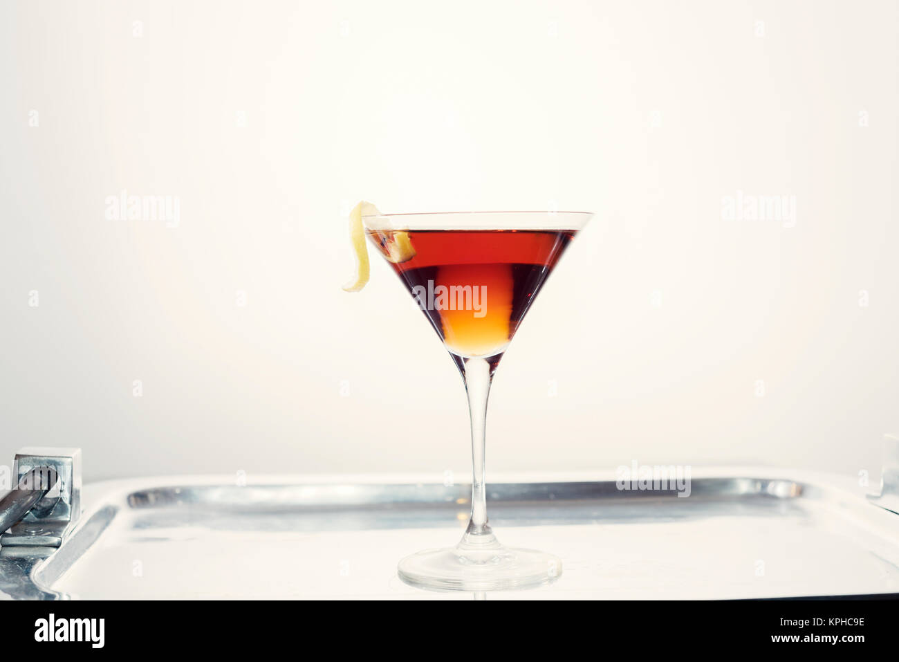 Single cocktail drink resting on silver serving tray with lemon twist ...