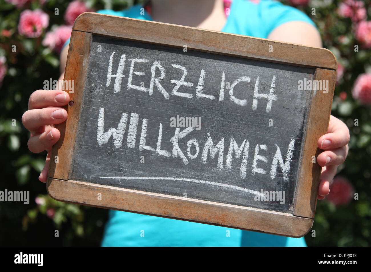 HERZLICH WILLKOMMEN (welcome in German) written with chalk on slate shown by young female Stock Photo