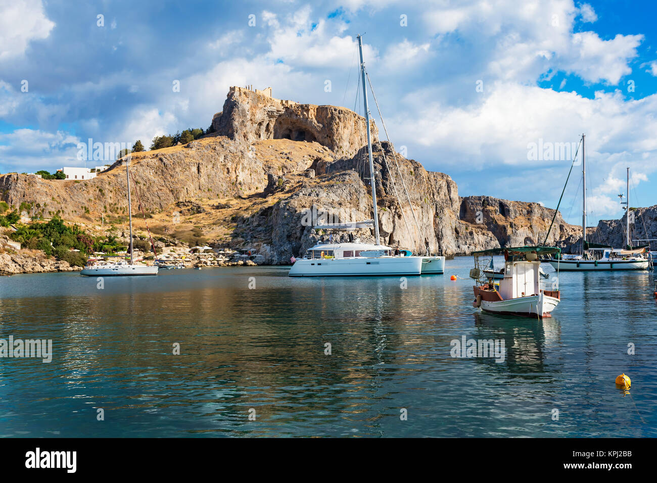 Fishing boats and sail boat in St. Paul´s bay, Lindos acropolis in background (Rhodes, Greece) Stock Photo