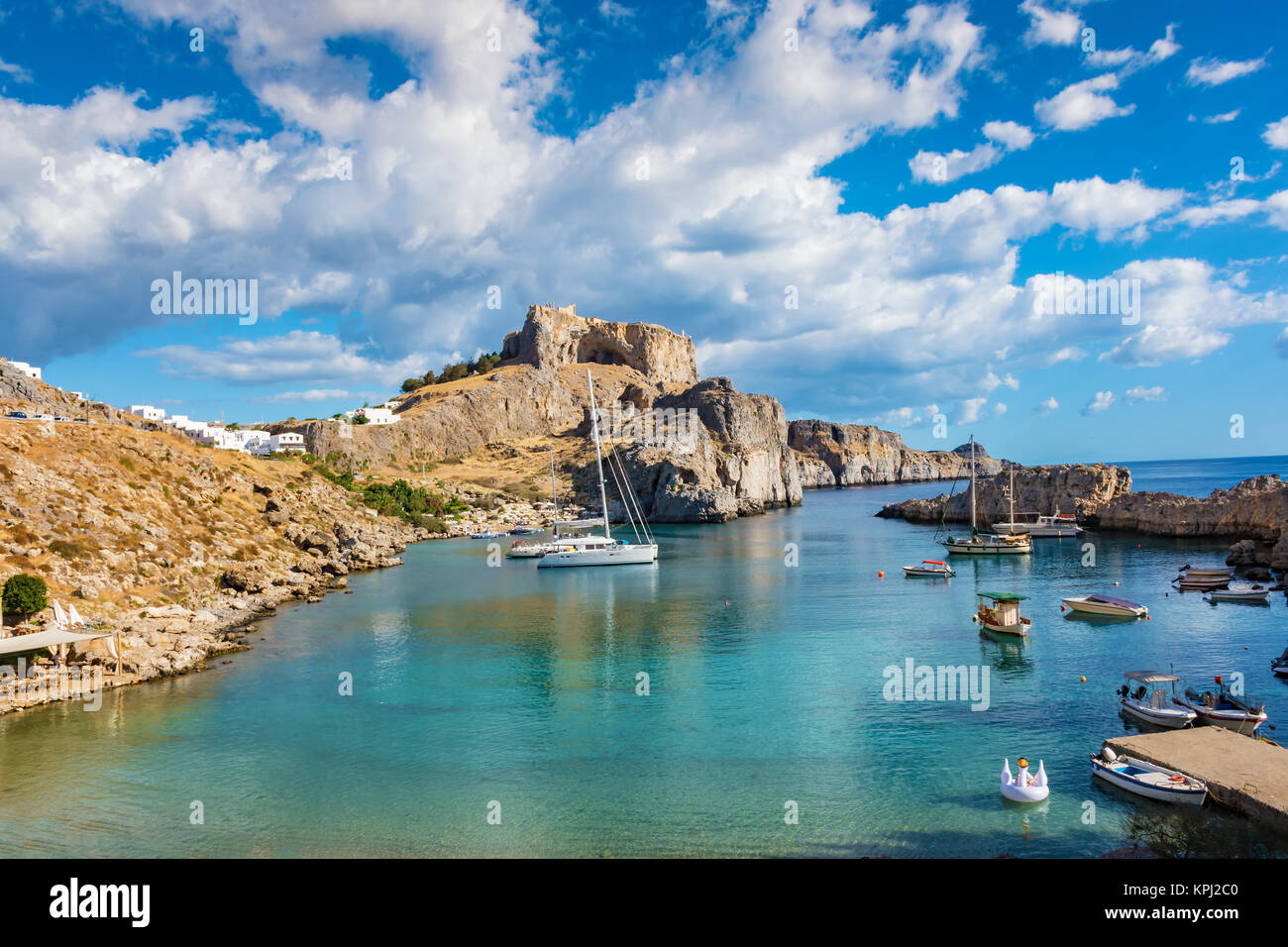 Fishing boats and sail boats in St. Paul´s bay, Lindos acropolis in background (Rhodes, Greece) Stock Photo