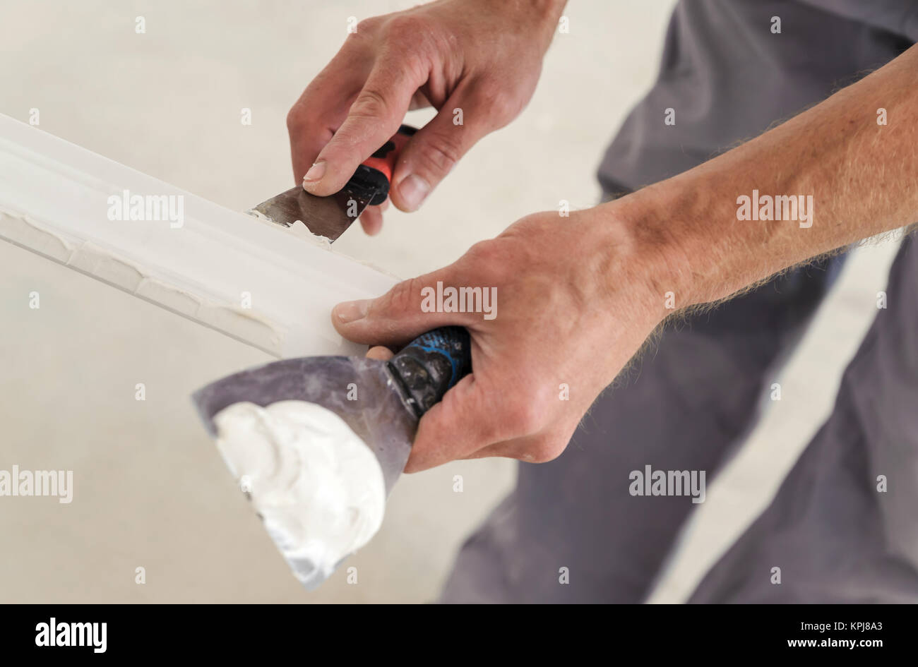 Installation of ceiling moldings. Worker puts glue on plastic molding