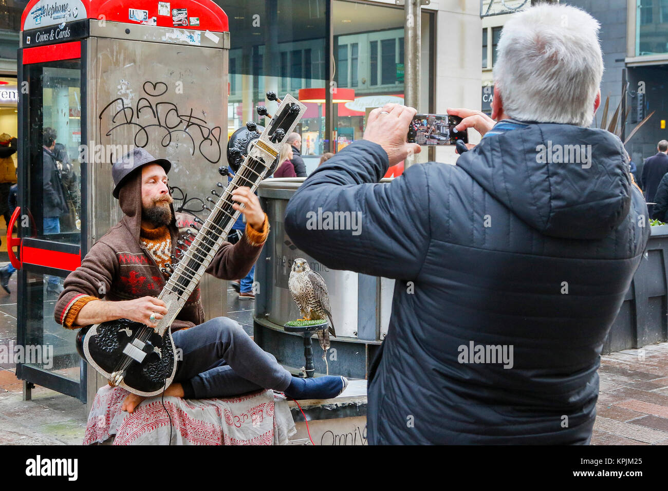 Glasgow, Scotland, UK. 16th December, 2017. As thousands of shoppers flocked to Glasgow city centre and in particular Buchanan Street also known as Glasgow's Style Mile many entered into the seasonal spirit and enjoyed the entertainment from the street musicians and buskers. PAUL JACKSON playing the sitar accompanied by his pet hawk Credit: Findlay/Alamy Live News Stock Photo