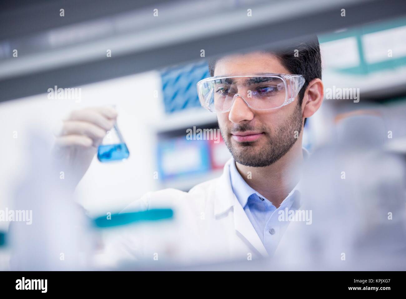 Laboratory assistant wearing safety goggles looking at chemical flask. Stock Photo