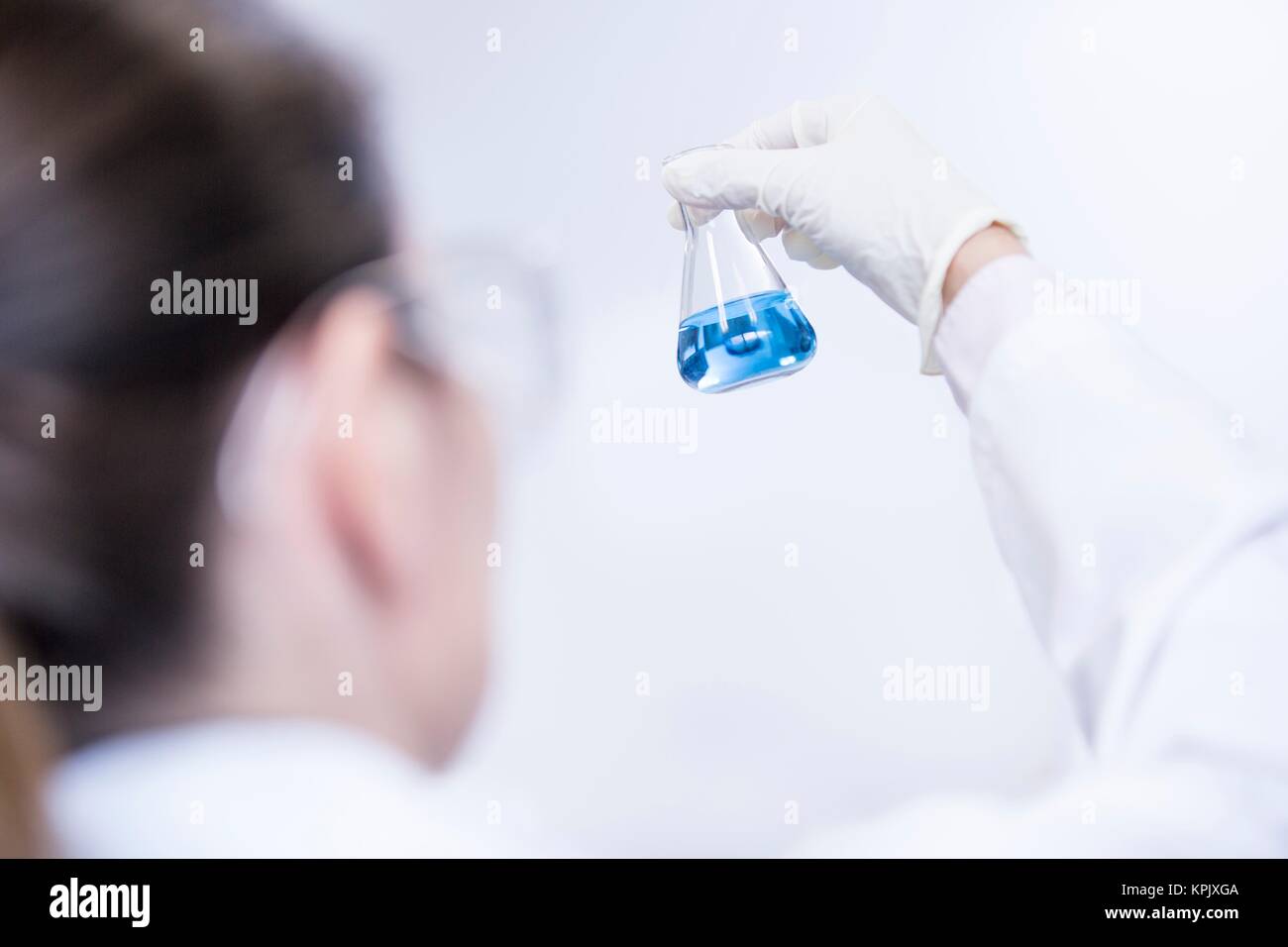Laboratory assistant holding chemical flask containing blue liquid. Stock Photo