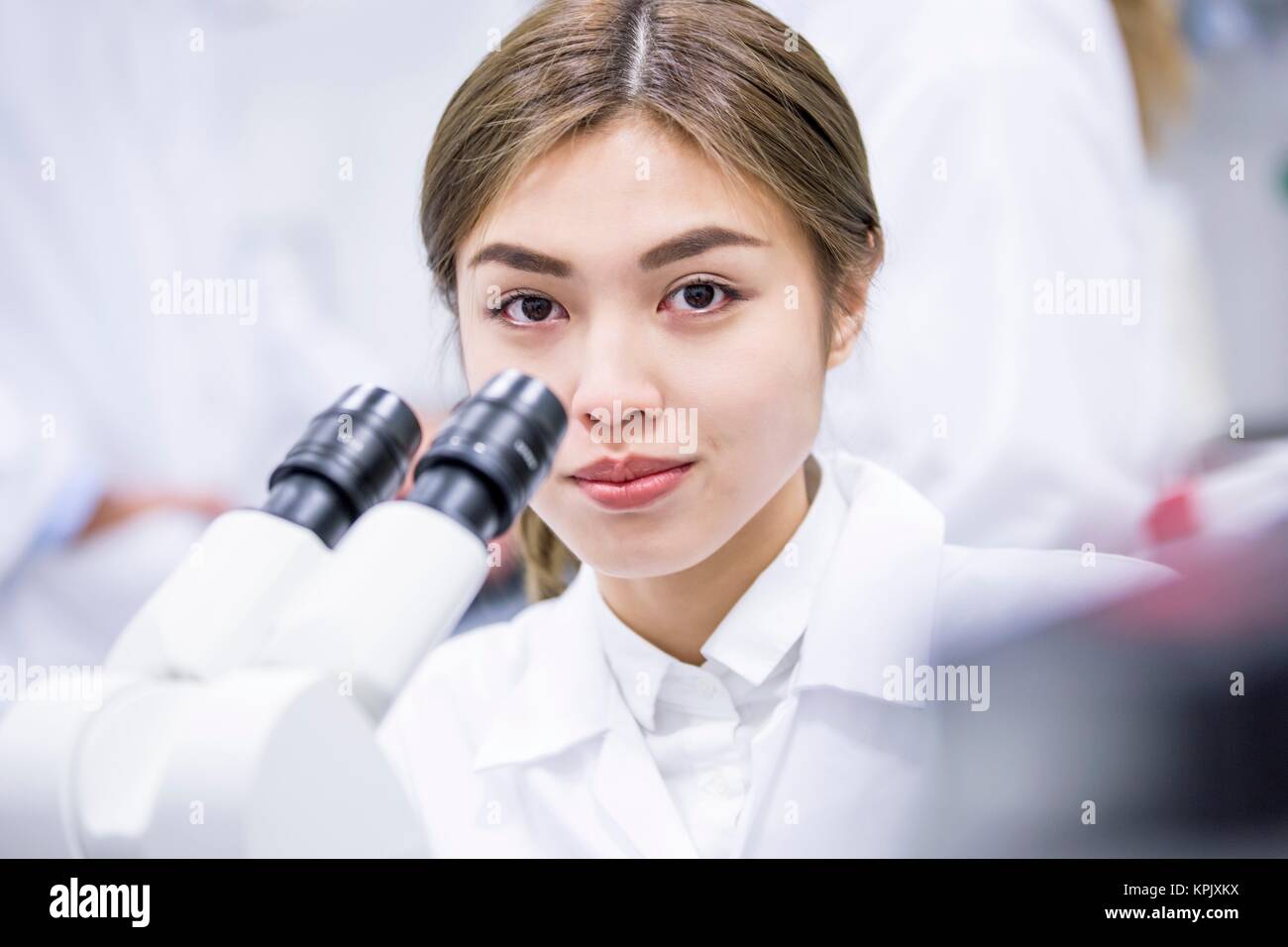 Female scientist using microscope, looking at camera. Stock Photo