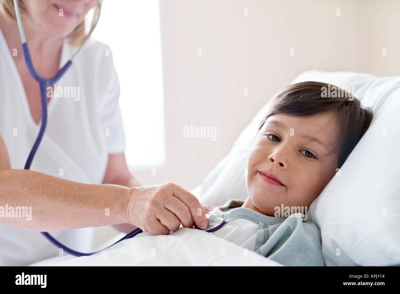 Young boy in hospital bed, nurse using stethoscope. Stock Photo